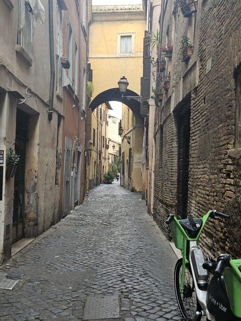 Narrow cobblestone street in Rome with historic buildings and a parked bike.