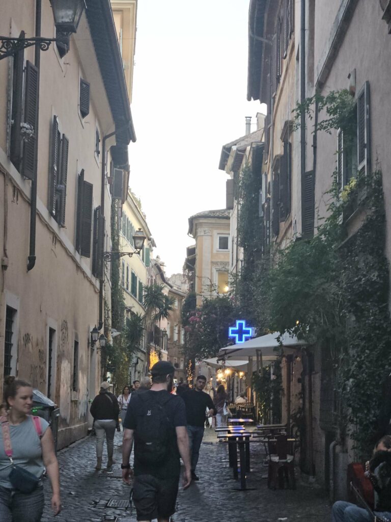 Narrow cobblestone street in Trastevere with people walking in the evening.